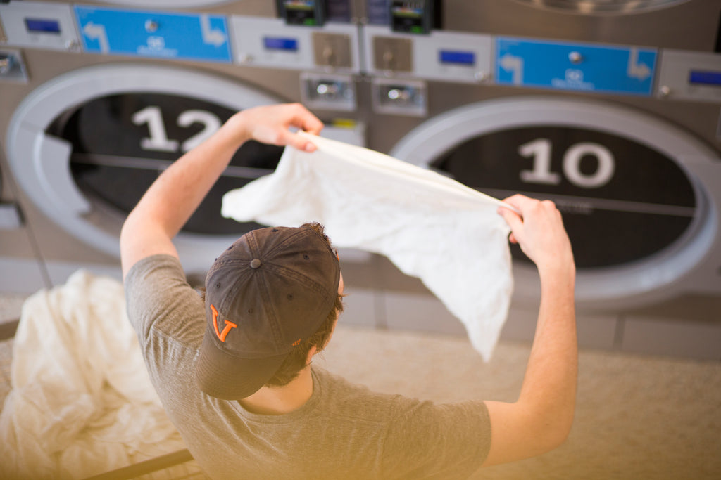 A college student (young man) wearing a baseball cap and doing laundry