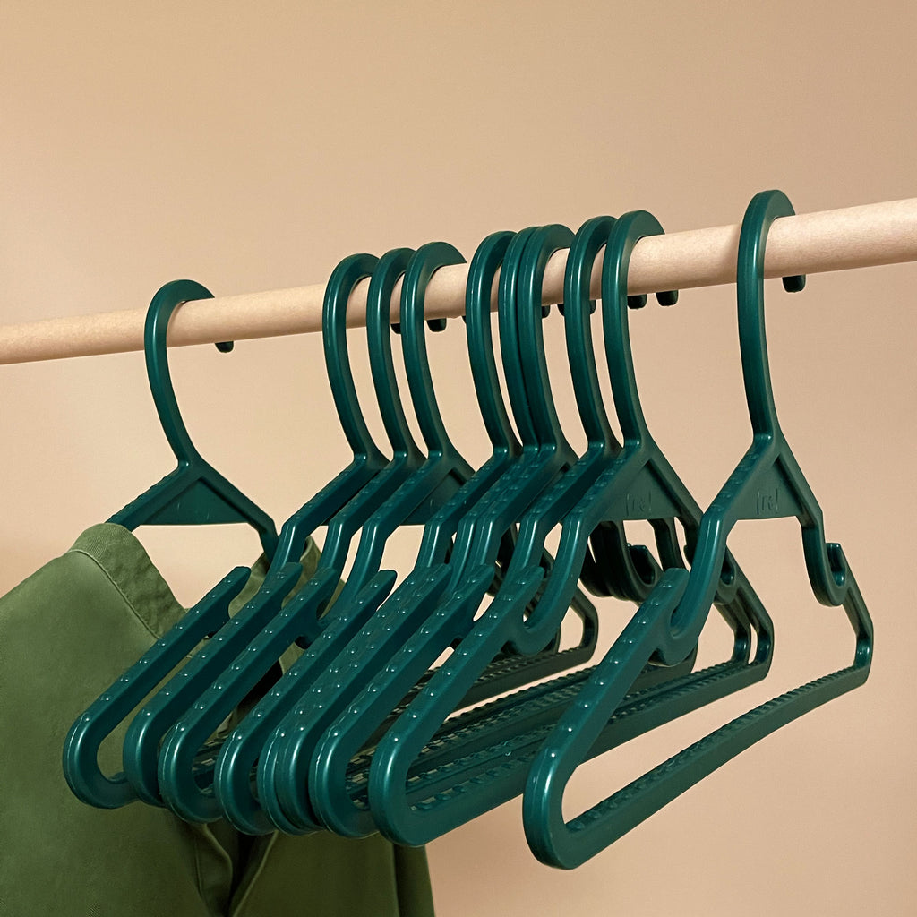 Pine green recycled ocean plastic hangers on a wooden pole; a seaweed green tunic hangs from one of the hangers