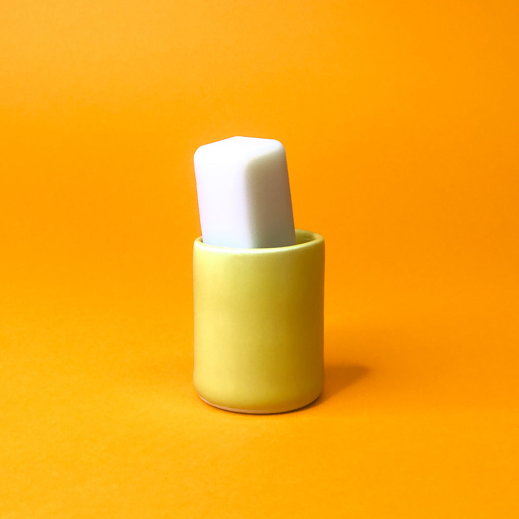 A white soap stick sits at an angle inside a tiny cylindrical yellow ceramic holder