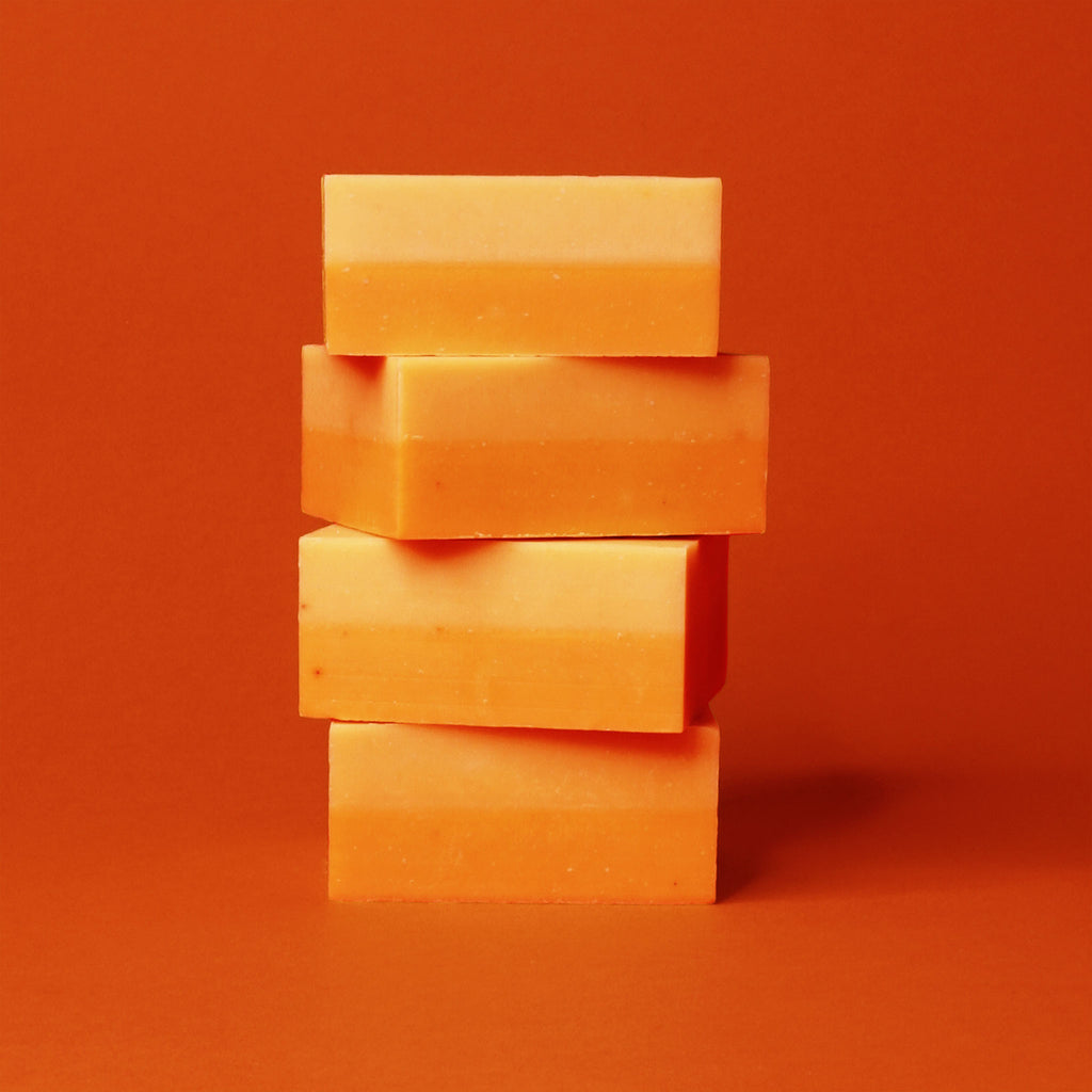A stack of two-tone yellow and orange soaps displayed with a blood orange backdrop