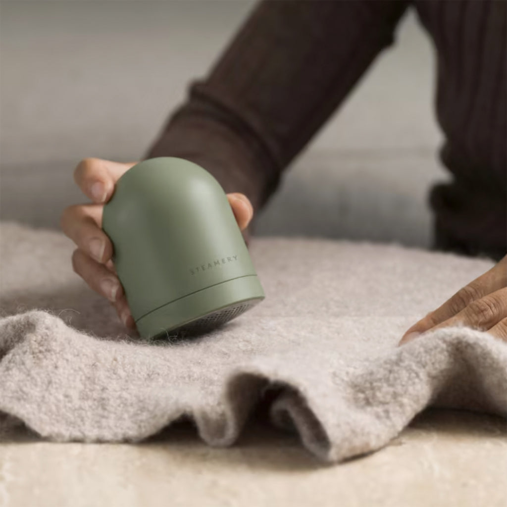 A hand uses a dome shaped fabric shaver on a winter sweater