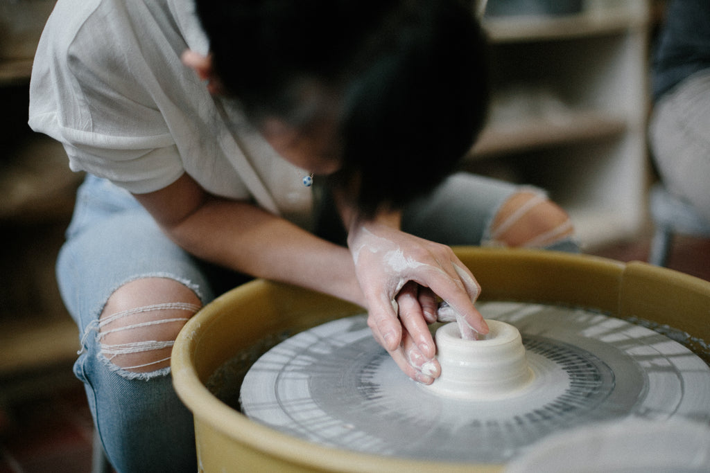 Suji Lee works on a small mound of clay on a wheel in a studio