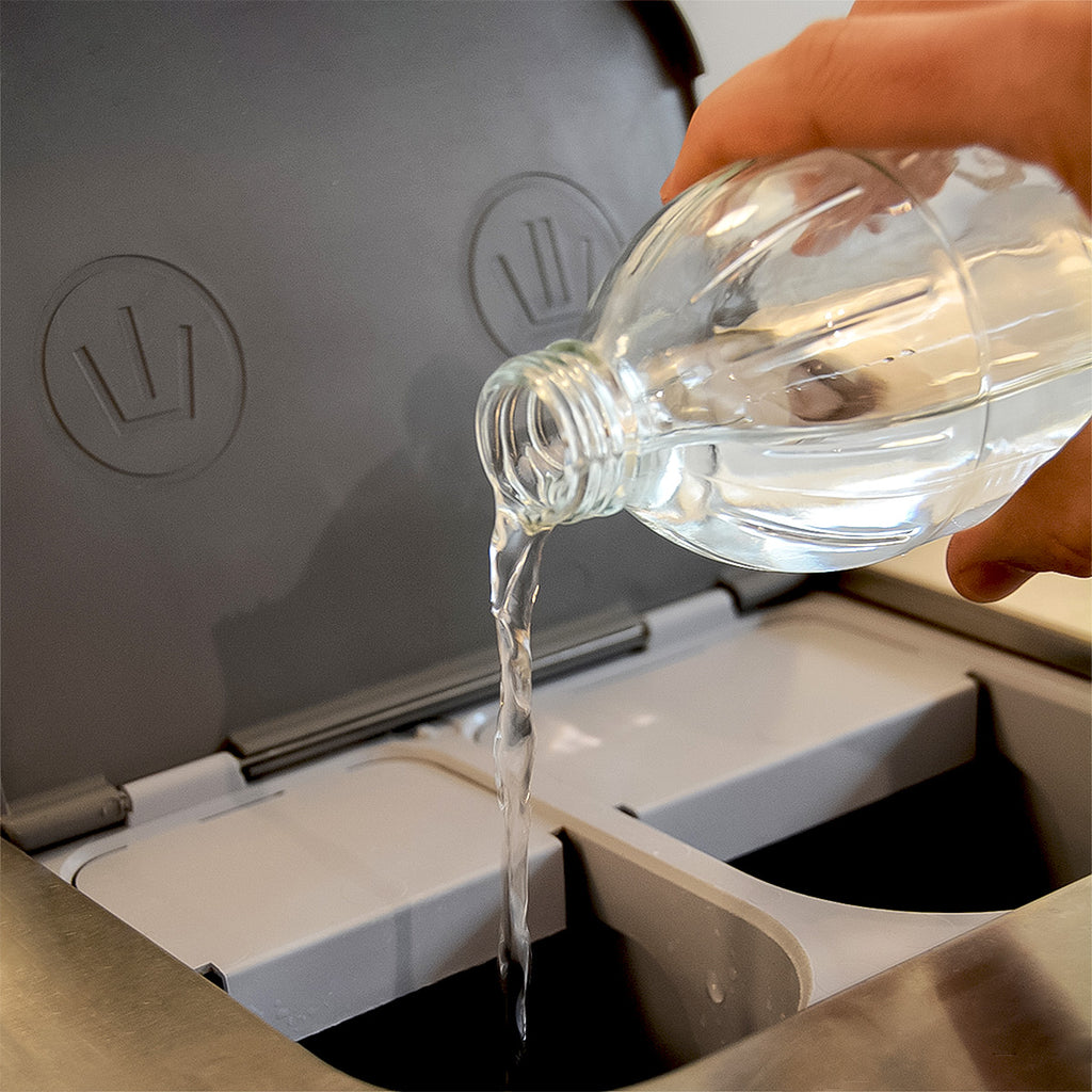 A hand pours distilled white vinegar into a compartment of a washing machine