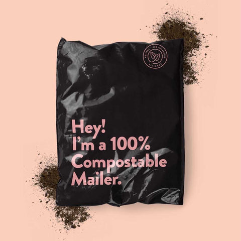 A black noissue compostable mailer reading "Hey! I'm a 100% Compostable Mailer." in pink text on a pink background with 2 piles of soil.