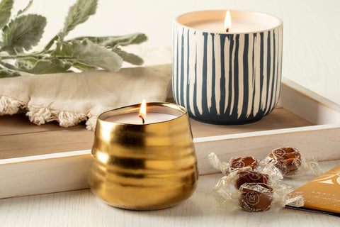 a blue and white striped candle with a gold candle from Prosperity Candle and some caramel candies on a white wood tray