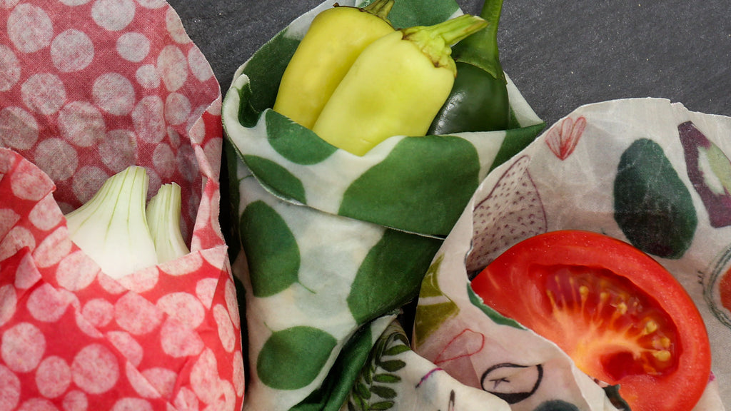 closeup of three veggie friends wrapped side by side: onion in connect the dots wrap, some green chilis in a leafy green wrap, and half a tomato in the farmer's market wrap