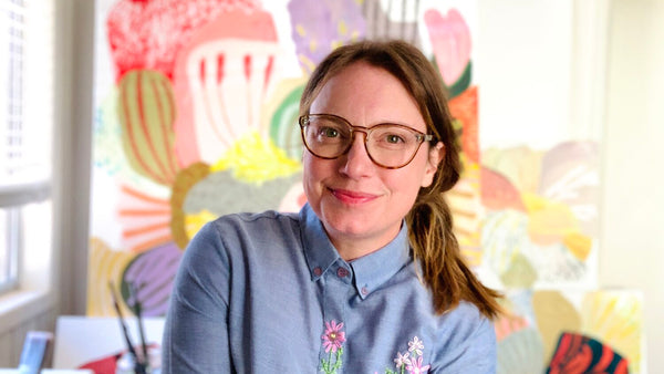 Illustrator Katie Vernon pictured in her colorful studio with her paintings behind her in the background