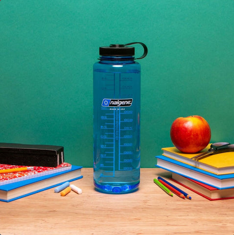 a blue 48oz nalgene wide mouth reusable water bottle in the center of a school desk