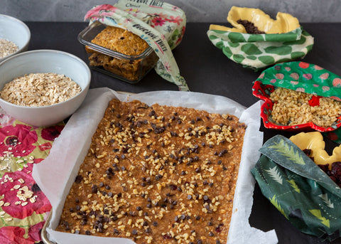 a tray of snack bars ready to bake, surrouned by ingredients and finished bars in the background