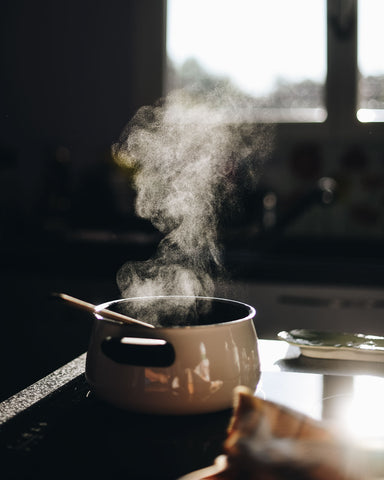 A steaming pot of food on a stovetop in the sunlight