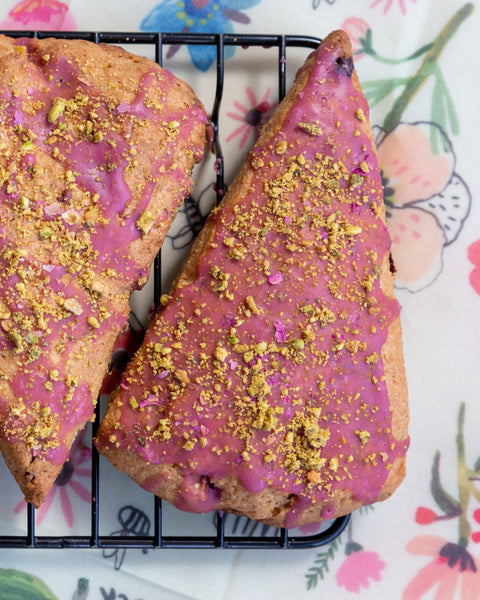 2 finished scones, frosted with a mauve icing and dusted with crushed pistachios and flower petals, sit on a rack on top of a Z Wrap beeswax wrap