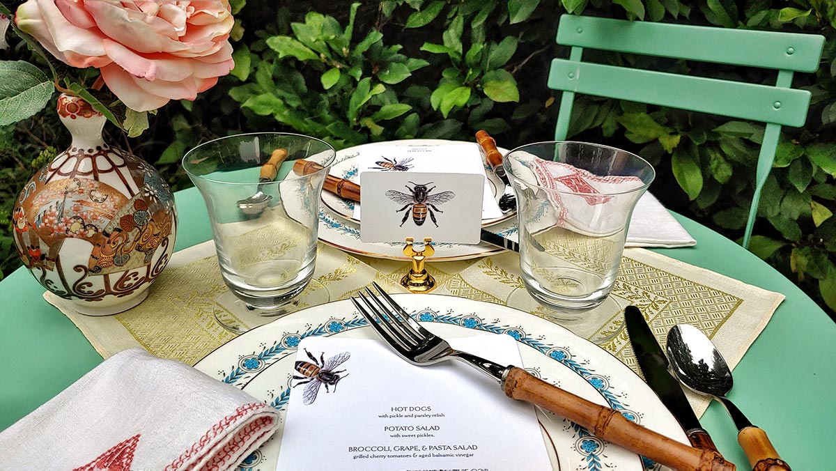 tea alfresco with green garden table for two, 'bees' illustrated place cards, bespoke menu cards, bamboo cutlery, and tea cups and bud vase