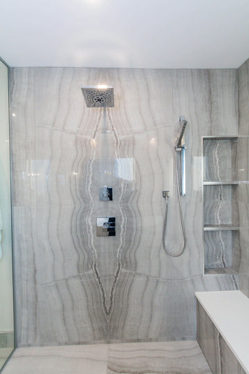 Grey travertine tiles, white shower bench top, and chrome plumbing fixtures.