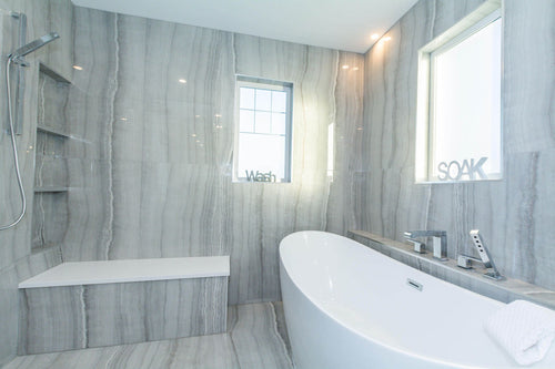 Grey travertine tiles, white quartz bench top, white freestanding tub, and chrome plumbing fixtures.