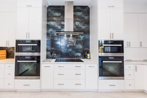 White lower cabinets and upper cabinets. White quartz countertop, stainless steel appliances, and grey metallic wall tile.