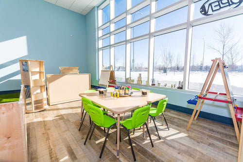 Light vinyl flooring, large windows, blue wall details, and light maple furniture with green chairs.