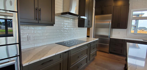 Dark grey kitchen cabinets, marble looking quartz, white textured subway tile, light grey and brown hardwood floor.