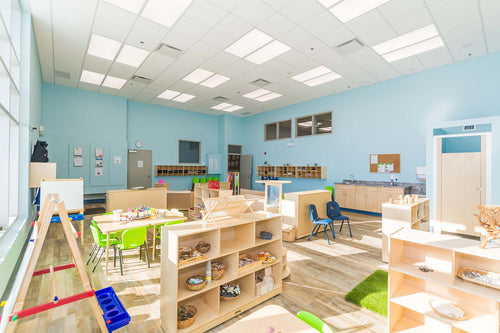 Light vinyl flooring, large windows, blue wall details, and light maple furniture with green chairs.