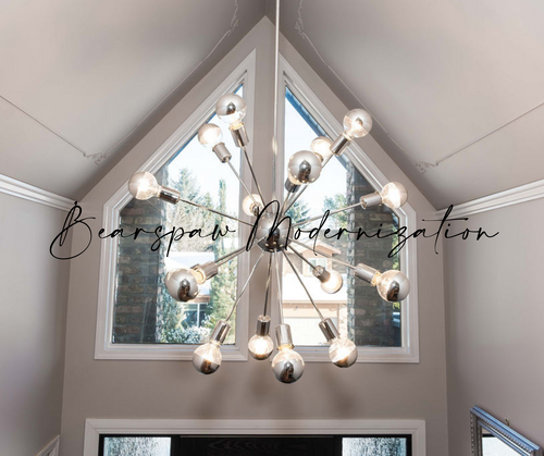 Chrome chandelier with chromed light bulbs hanging in a gray vaulted foyer.