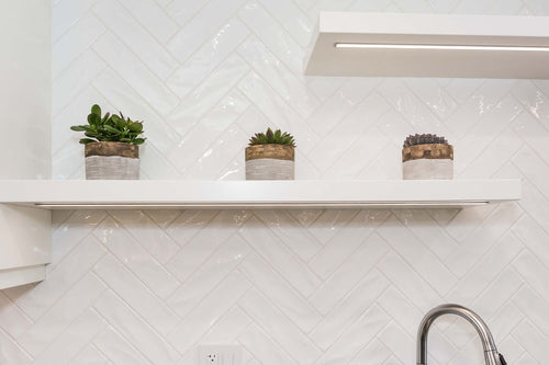 White floating shelves with under cabinet lighting, white rectangle herringbone tile.