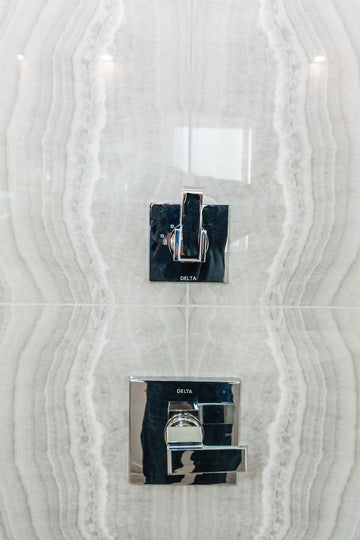 Grey travertine tiles, white freestanding tub, and chrome plumbing fixtures.