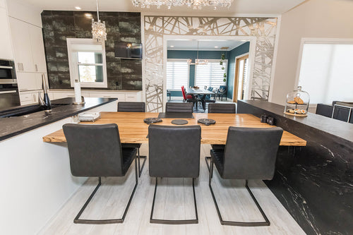 White lower cabinets and upper cabinets. White quartz perimeter countertop, black granite countertop, wood dining table, grey metallic wall tile, and grey metal abstract entrance detail.