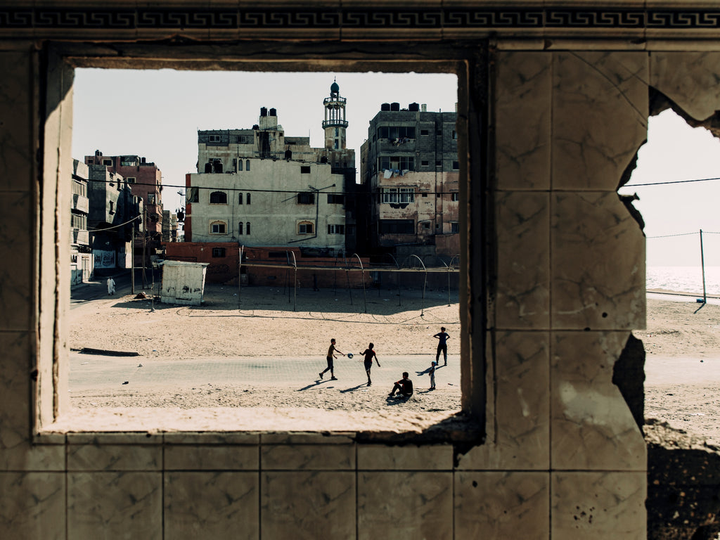 A window into the world of people in crisis - children play football on the beachfront in Gaza to a back drop of a shelled building. © Paddy Dowling/EAA