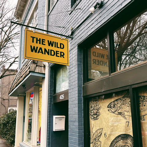 Gazing up at a gray-blue shop exterior you see a bright yellow hand painted sign with The Wild Wander in brown letters