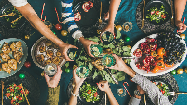 Hands reach across a table laden with food to raise a glass in cheers