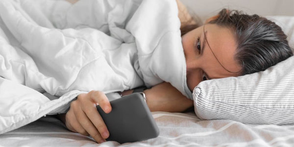 A woman snuggled in bed, scrolling on her smart phone.