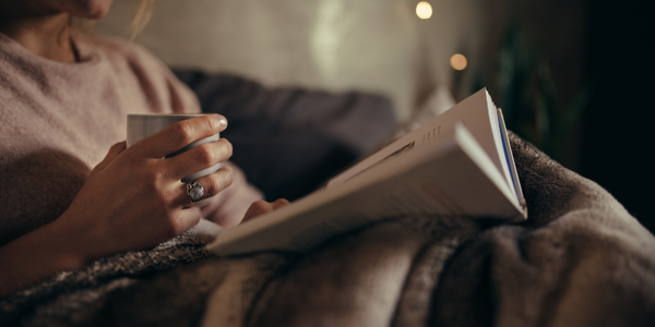 A person reading an open book while holding a hot cup of tea.