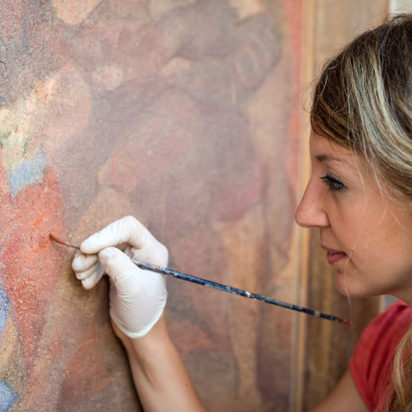 An art restorer meticulously works on an oil painting