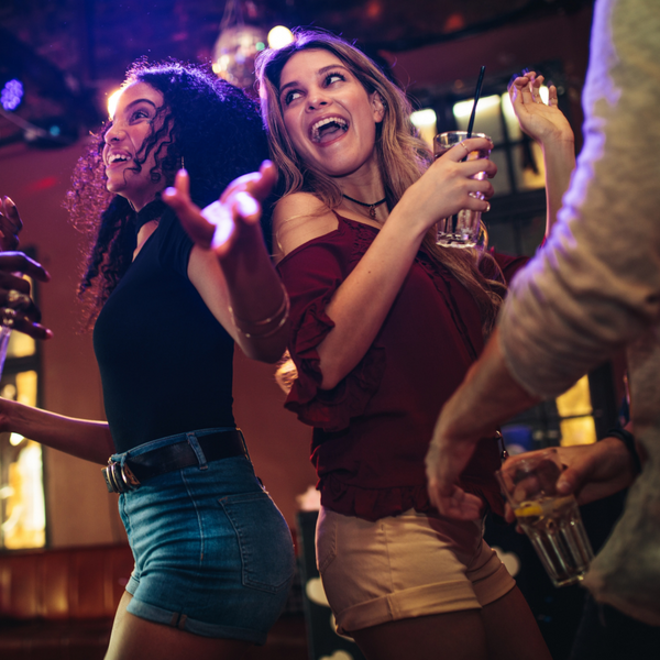 Two friends dancing, having a laugh and a drink at a club