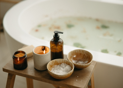 A bathtub filled with botanicals and a small table with bathing essentials and a lit scented candle.