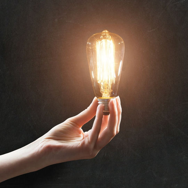 A hand holds a lit-up Edison bulb.