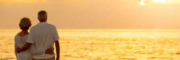 A senior couple embrace on the beach while watching the sun set.