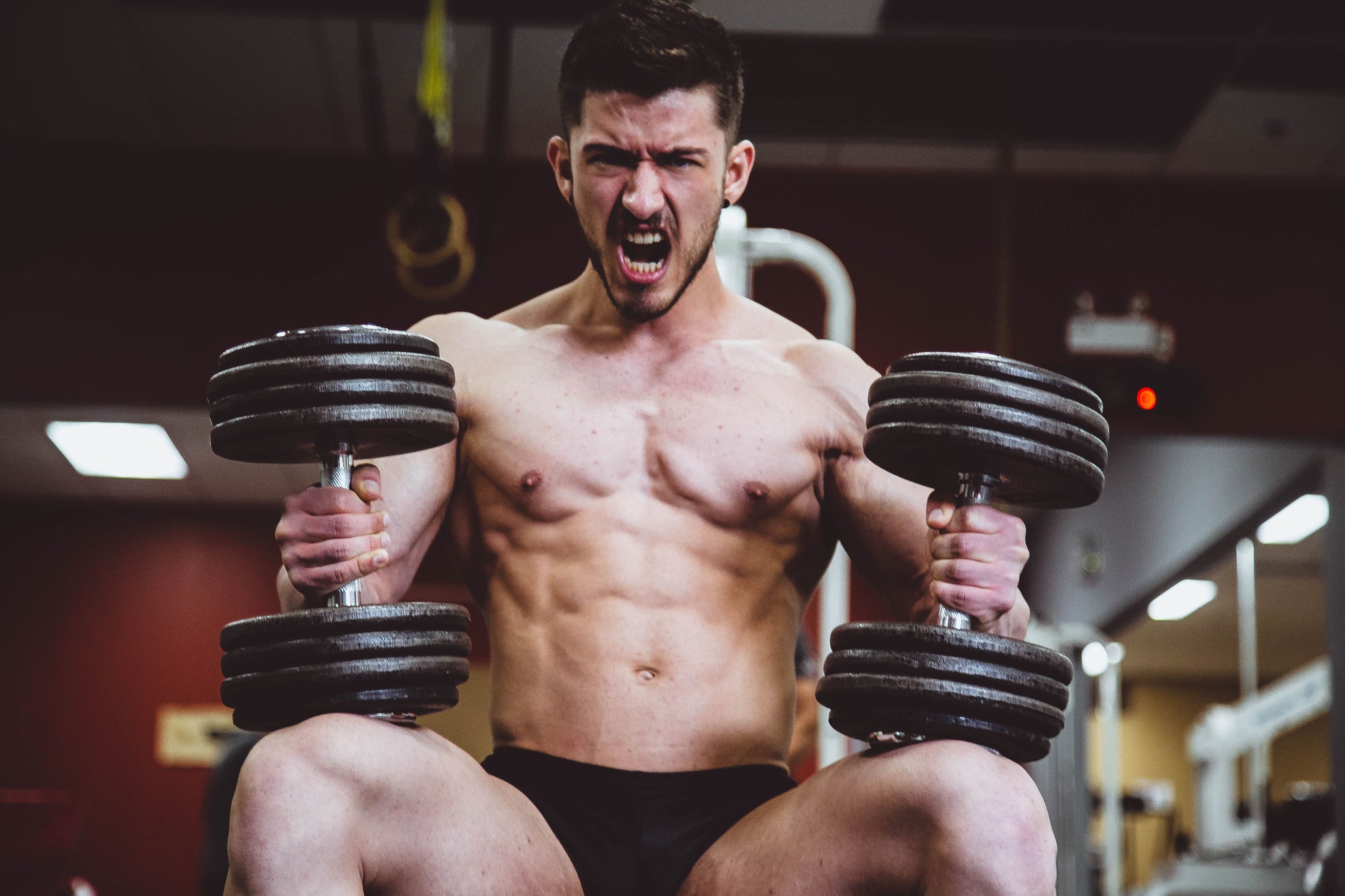 Athlete lifting weights with his mouth agape in a gym
