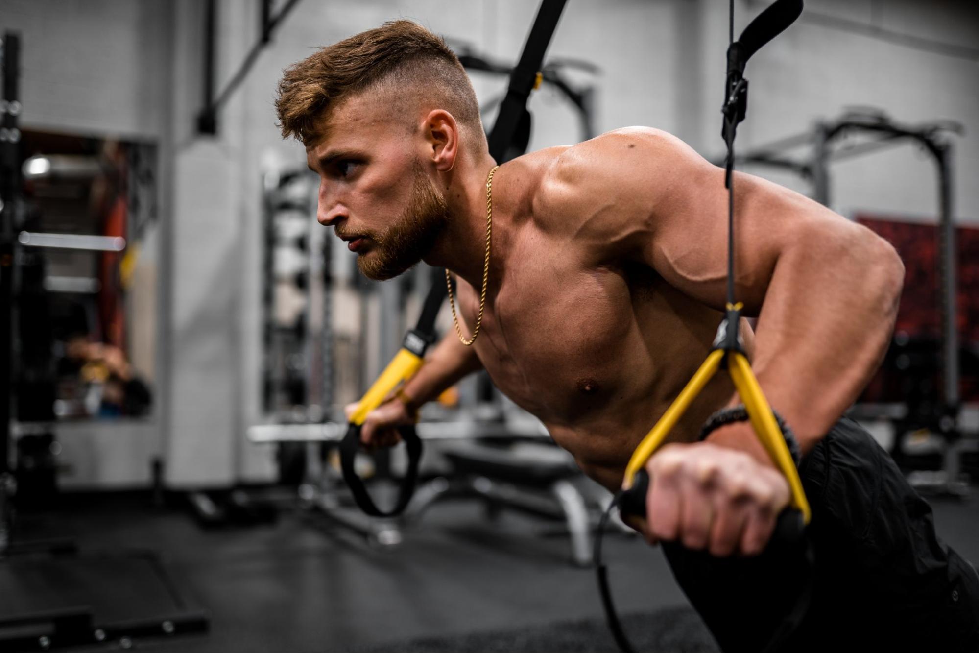 Athlete powered by two protein shakes a day is performing push-ups using yellow resistance bands to strengthen his arms and upper body