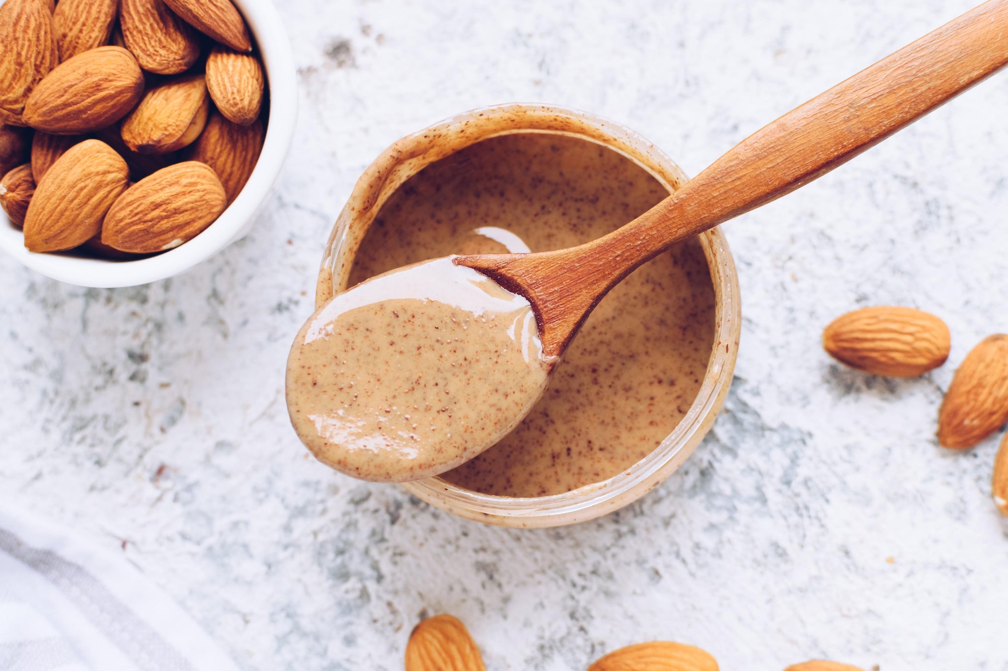 Almonds and wooden spoon with nut butter placed on top of nut butter jar