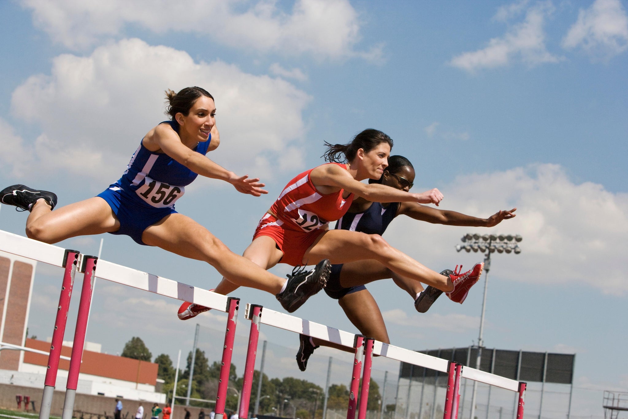 Three competitive female athletes who took liquid protein shots prior to the competition jump over a hurdle