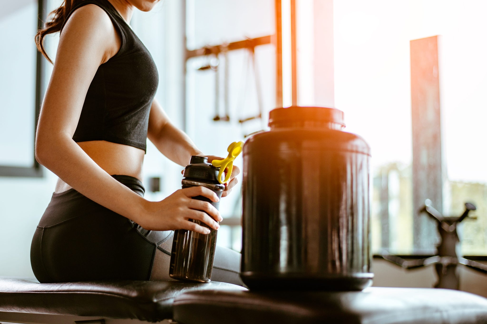 Female athlete holding a tumbler with easy to digest protein shake while resting at a gym after working out