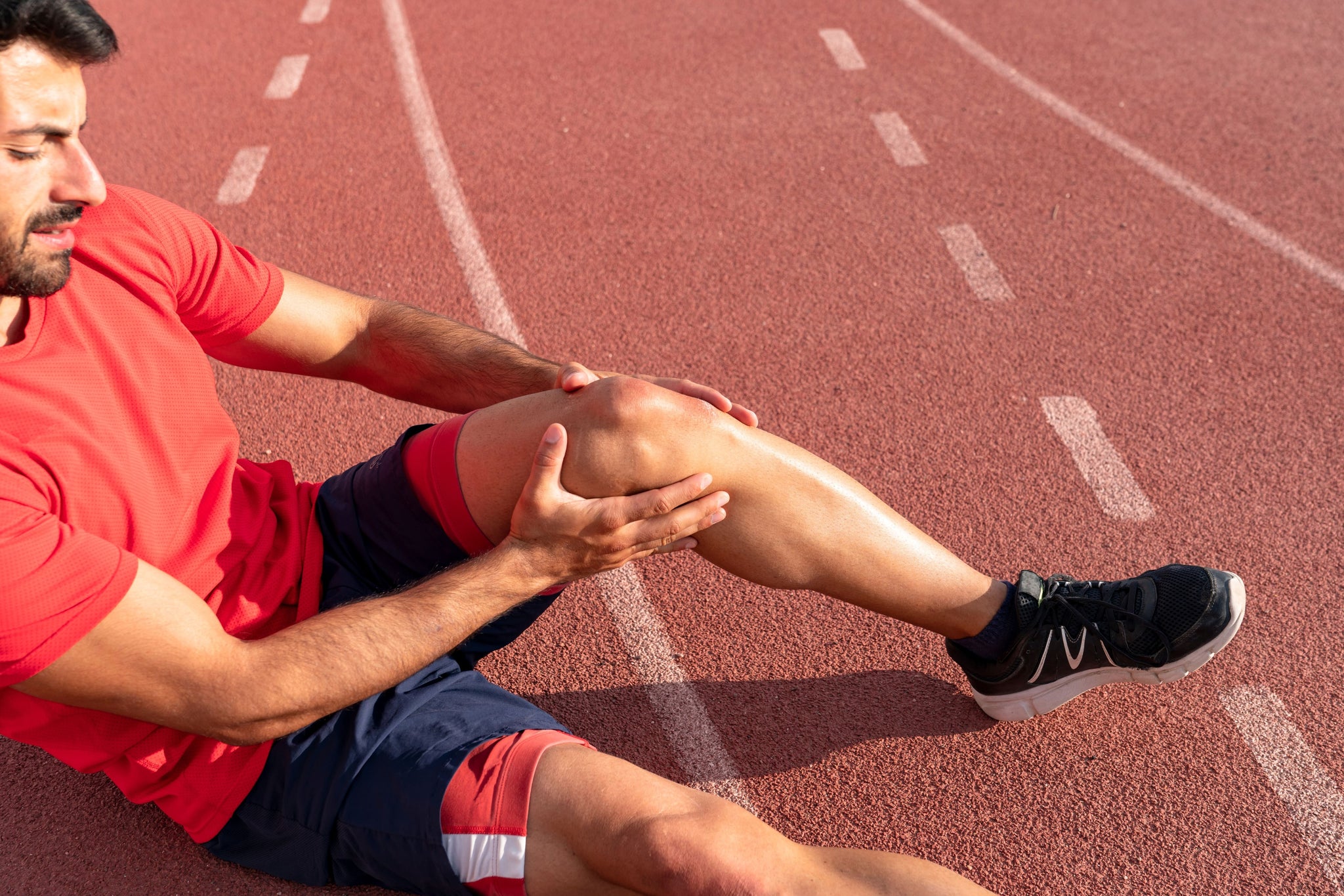 Male athlete holding his injured knee while wondering, “How long does a torn ACL take to heal?”