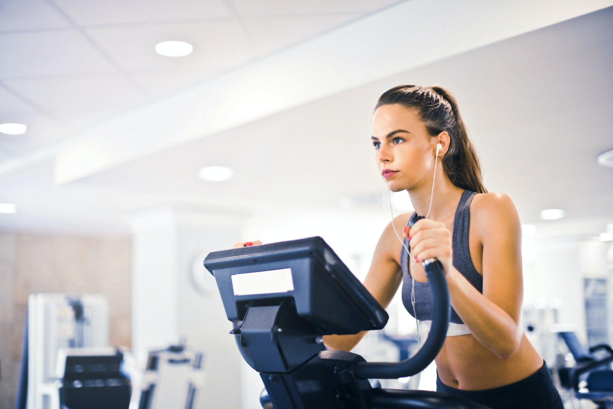 Female athlete tuning in to a podcast on the benefits of collagen peptide protein while running on a treadmill in a modern gym