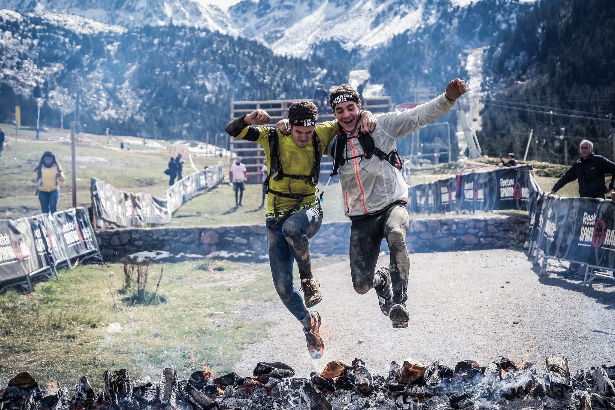 Two spartan racers, who know what the benefits of taking collagen are, jump over a heap of hot coals