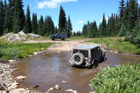 jeep in muddy trail water on sunny day