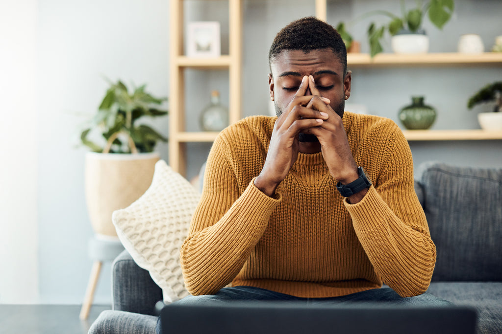 black man sitting on couch holding his sinuses fighting a cold or virus