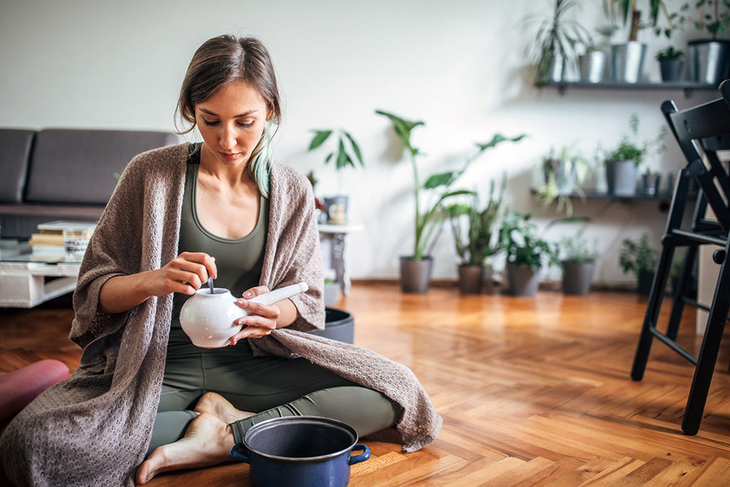 woman sitting on floor preparing a neti pot - spring seasonal allergy relief