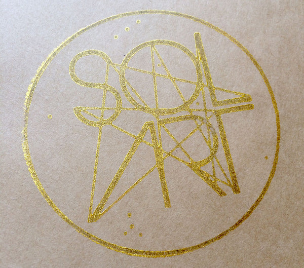 A gold stamp of Solart's first logo design, stamped onto brown recycled kraft paper.