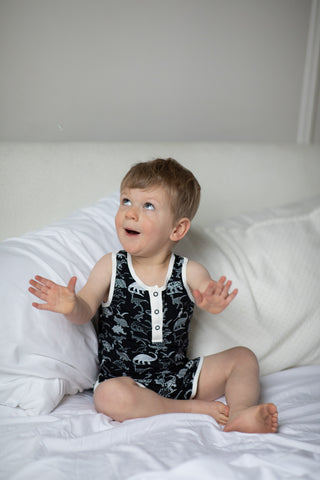 A young boy wears black dinosaur pajamas while making a surprised face