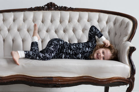 A girl wearing dinosaur pajamas lays on a bench